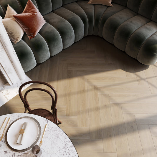 Detail van een stijlvolle visgraat PVC-vloer van Commando Vloeren in een sfeervolle zithoek met een marmeren tafel en een fluwelen bank, ideaal voor een moderne en warme woonomgeving.